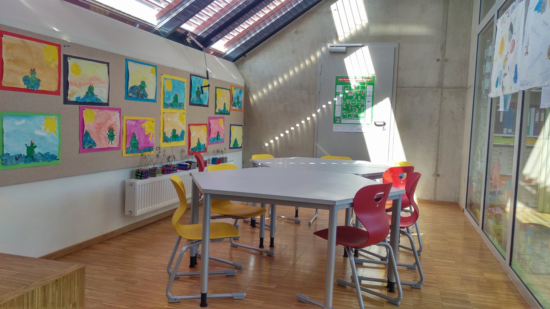 Ein kleiner Klassenraum für Gruppenarbeiten, Lernstunden oder gemeinsamen Gesprächen . Bunte ergonomische Sessel und eine Pinwand für Notizen sind an der Wand zu finden. Bilder der Schüler Volksschule Brockmann verzieren zur Zeit die Wand